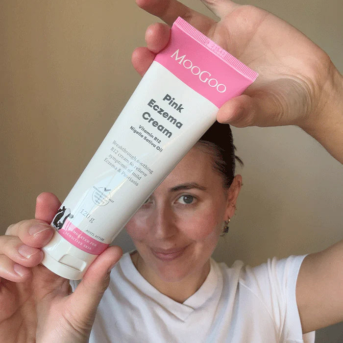 woman smiling holding a tube of MooGoo Pink Eczema Cream in front of her face.