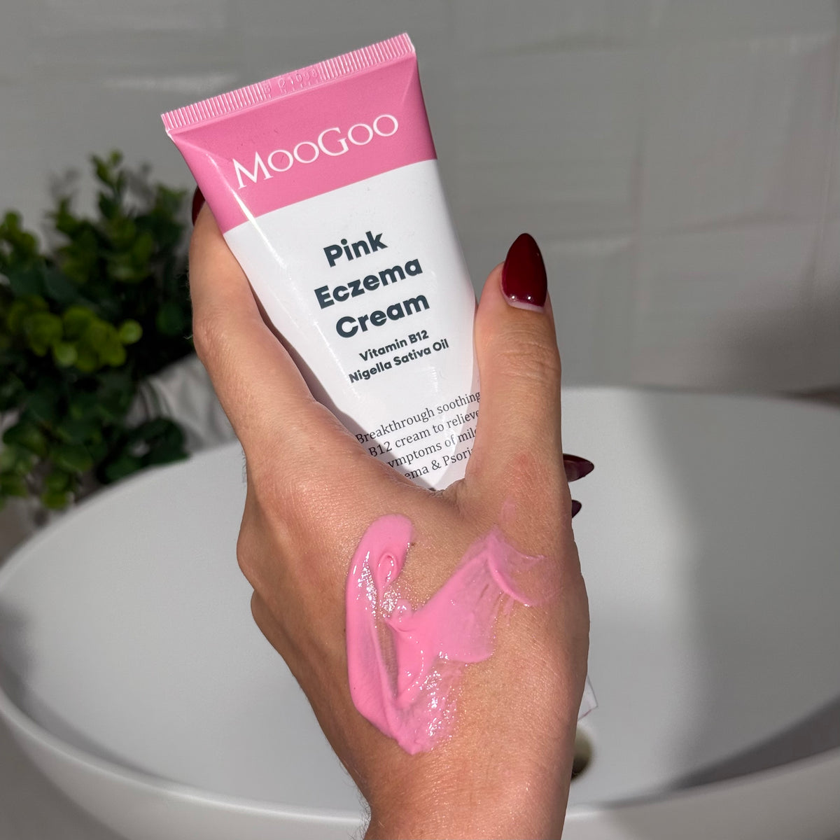 Hand holding a tube of MooGoo Pink Eczema Cream with visible pink cream on hand.